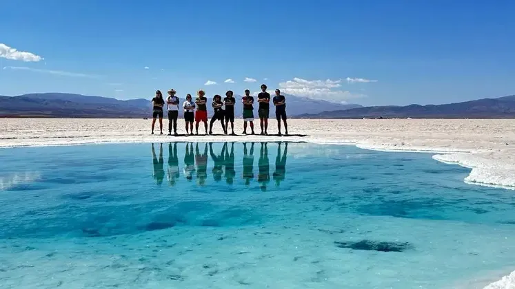 Un viaggio di gruppo WeRoad si riflette in una piscina turchese su una vasta distesa salina sotto un cielo azzurro e limpido.