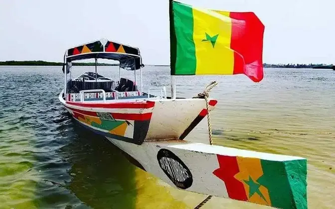 Ein farbenfrohes Boot mit der senegalesischen Flagge am Bug schwimmt in ruhigem Wasser.