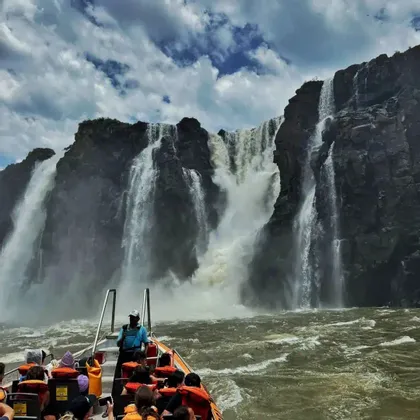 Un viaggio di gruppo WeRoad in barca si dirige su acque agitate verso un'imponente cascata che si getta da una scogliera rocciosa.
