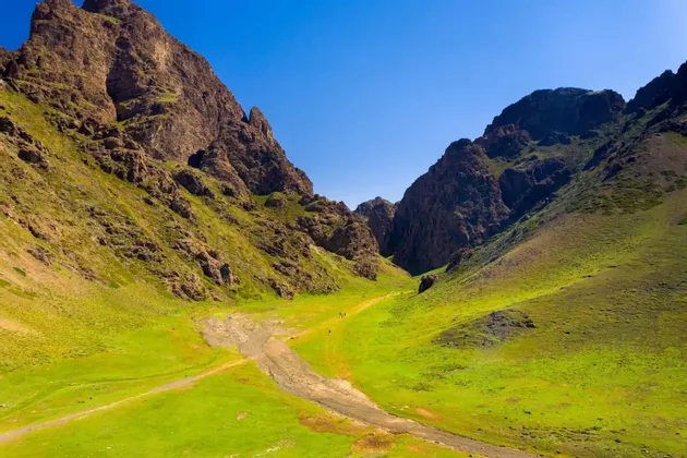 Un viaggio di gruppo WeRoad percorre un sentiero in un'ampia valle verde tra montagne rocciose, sotto un cielo azzurro limpido.