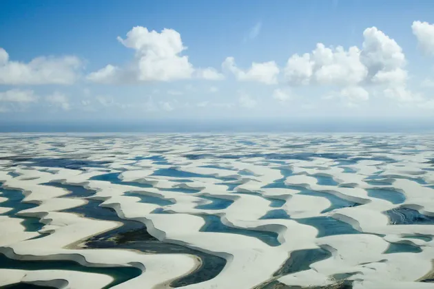 Una vista aerea di vaste dune di sabbia bianca piene di lagune di acqua blu sotto un cielo parzialmente nuvoloso.