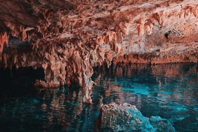Stalattiti marrone-rossastre pendono sulla superficie di acqua cristallina e turchese all'interno di una grotta sotterranea.