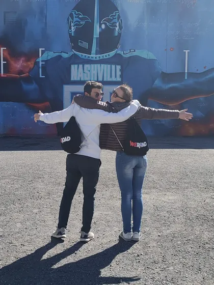 Un uomo e una donna di un viaggio di gruppo WeRoad si abbracciano a braccia aperte davanti a un grande murale di football americano a Nashville.