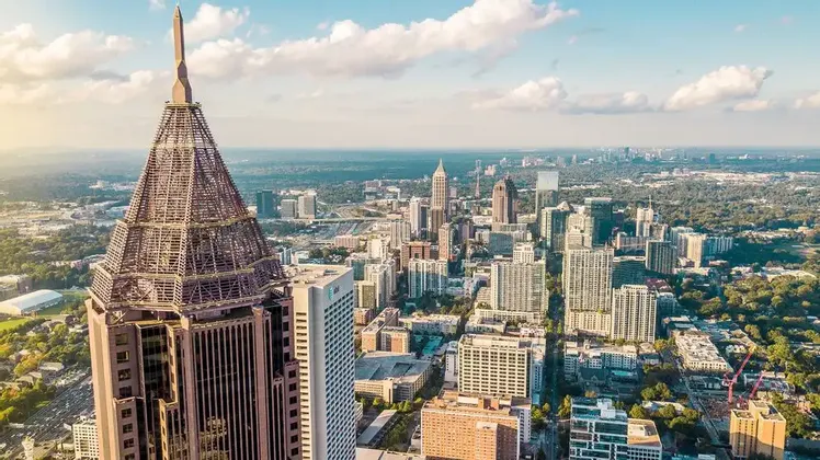 Una vista aerea dello skyline di una vasta città, con un alto edificio e la sua caratteristica guglia prominenti in primo piano.