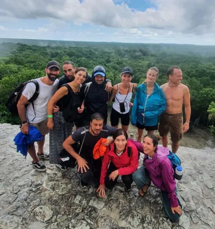 Un gruppo WeRoad in viaggio posa per una foto su un punto panoramico roccioso, con una vasta foresta verde che si estende sotto un cielo nuvoloso.