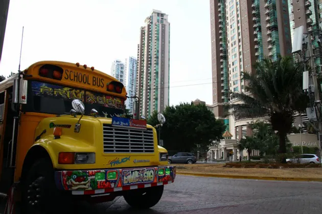 Un bus scolaire jaune, décoré de graffitis colorés, est garé dans une rue de ville devant de hauts bâtiments modernes.