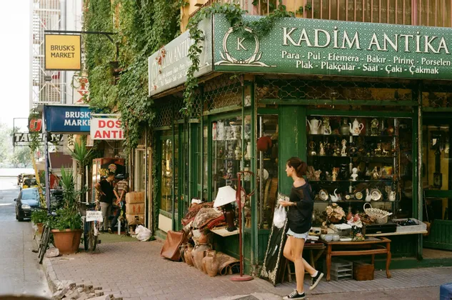 Una donna passa davanti a un negozio di antiquariato su una strada cittadina, con vari oggetti esposti sul marciapiede.