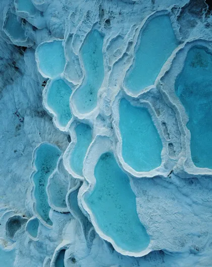 Vista aerea di piscine di acqua turchese incastonate in terrazze di travertino bianco a cascata.