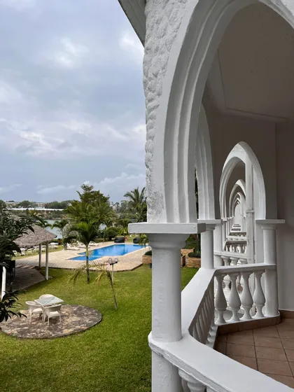 Una vista dal balcone di un resort attraverso una serie di archi bianchi, che si affaccia su un giardino con piscina.