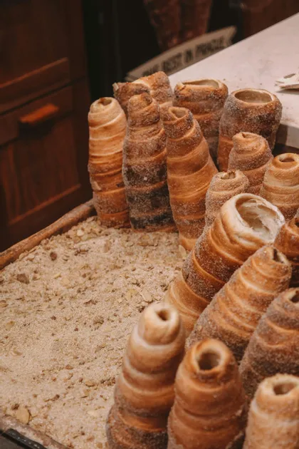 Primo piano di diversi dolci conici, Trdelník, ricoperti di zucchero e disposti verticalmente in un vassoio espositore.