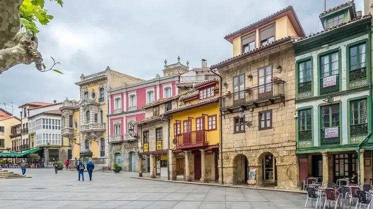 Edificios coloridos de varios pisos con arquitectura variada bordean una gran plaza adoquinada bajo un cielo nublado.