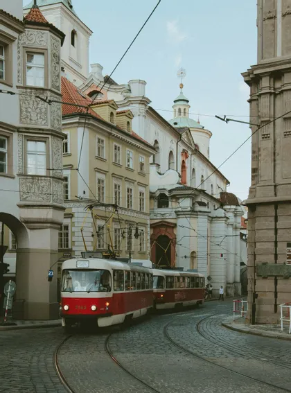 Un tram rosso e bianco percorre i binari lungo una via acciottolata e tortuosa, fiancheggiata da edifici storici e decorati.