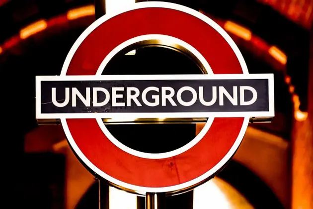 Un primo piano dell'iconico segno a bersaglio della metropolitana di Londra, che risplende su uno sfondo caldo, scuro e sfocato.