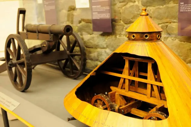 Un modello in legno sezionato del veicolo corazzato di Leonardo da Vinci accanto a un modello di cannone in una mostra museale.