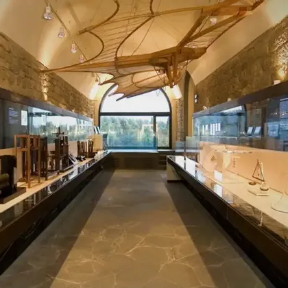 Una sala espositiva di un museo con teche di invenzioni e un grande modello di macchina volante in legno sospeso dal soffitto a volta.