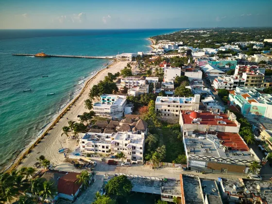 Una vista aerea di una città costiera con una spiaggia sabbiosa e un lungo molo che si estende nell'oceano turchese