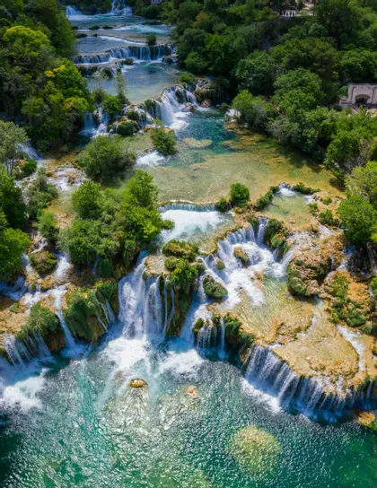 Una vista aérea de cascadas que fluyen a través de un exuberante bosque verde hacia piscinas de color turquesa claro.