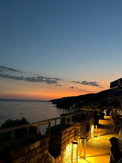 Una vista da una terrazza in pietra illuminata con affaccio sul mare e sulla costa in silhouette al tramonto.