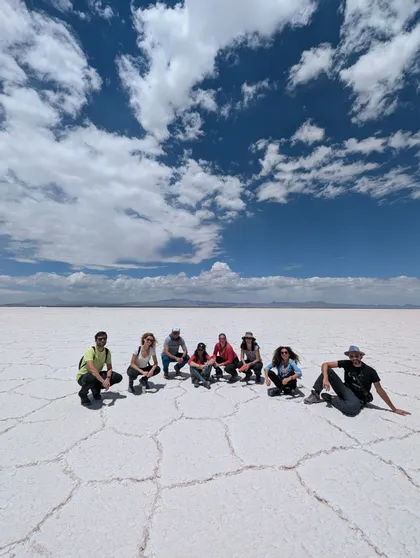 Un grupo de WeRoad posando en un extenso salar blanco bajo un cielo azul con nubes dispersas.