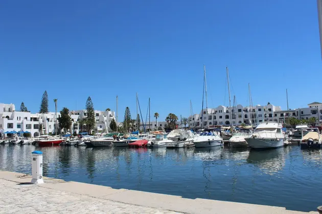 Un porto turistico pieno di barche e yacht ormeggiati di fronte a edifici bianchi in una giornata di sole.