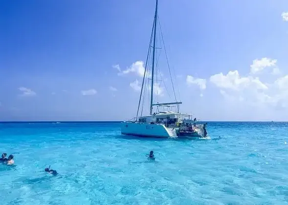 Eine WeRoad-Gruppe schwimmt und schnorchelt an einem sonnigen Tag in klarem türkisfarbenem Wasser neben einem weißen Katamaran.