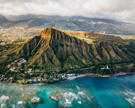 Una vista aerea di una grande montagna frastagliata su una costa tropicale, dove l'acqua turchese incontra una riva fiancheggiata da edifici.