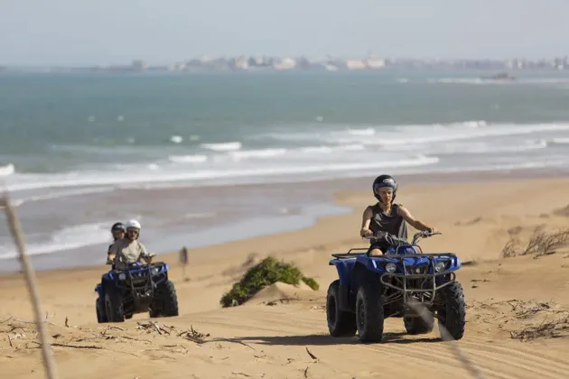Eine WeRoad-Gruppenreise beim Quadfahren auf Sanddünen entlang eines Strandes mit dem Ozean im Hintergrund.