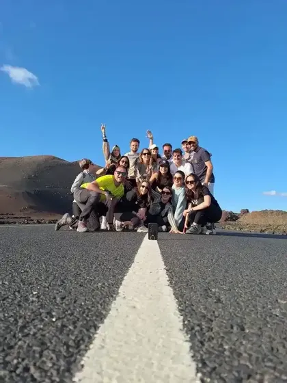 Un viaggio di gruppo WeRoad in posa per una foto su una strada deserta, con colline scure e un cielo azzurro chiaro sullo sfondo.