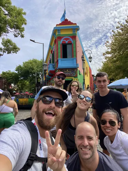 Un gruppo WeRoad in viaggio sorride e si fa un selfie su una strada cittadina davanti a un edificio multicolore.