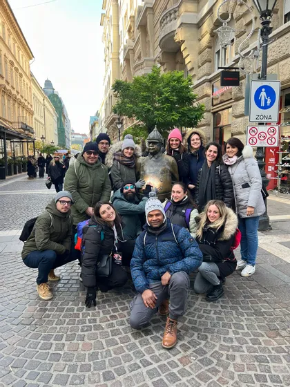 Un viaje en grupo de WeRoad con ropa de invierno posando para una foto grupal con una estatua de bronce en una calle adoquinada de la ciudad.