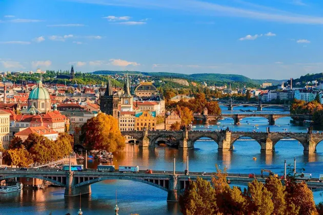 Une vue panoramique d'une ville européenne en automne, avec plusieurs ponts enjambant une rivière sous un ciel bleu clair.