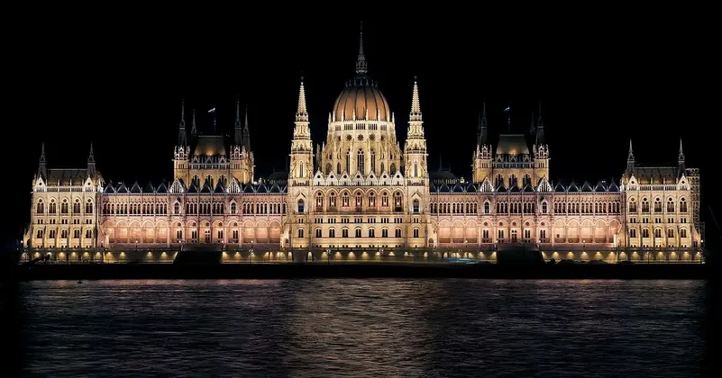 Un grand bâtiment orné d'un dôme central est brillamment éclairé la nuit à travers un plan d'eau.