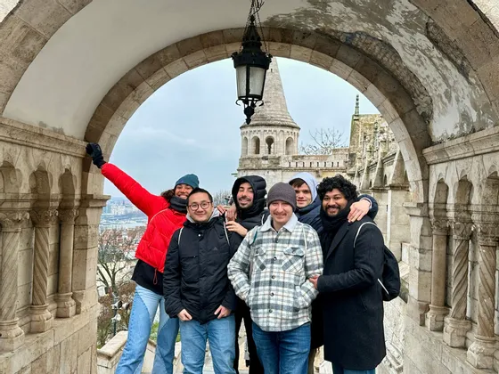 Un voyage de groupe WeRoad de six personnes souriant ensemble sous une arche en pierre, avec un bâtiment historique en arrière-plan.