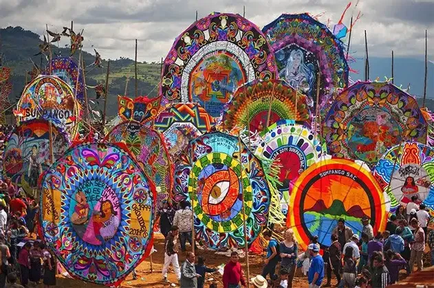 Aquiloni giganti, colorati e finemente dipinti sono esposti a una folla durante un festival all'aperto, con colline sullo sfondo.