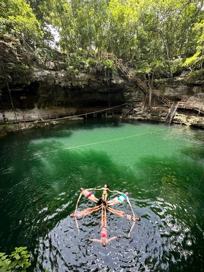Eine WeRoad-Gruppe bildet eine Sternform, indem sie händchenhaltend im smaragdgrünen Wasser einer Cenote treibt.
