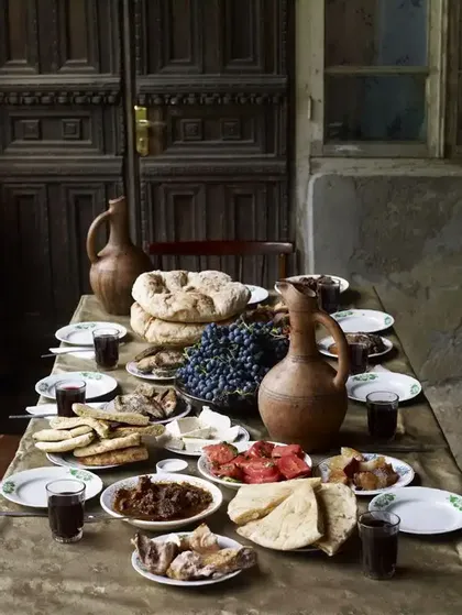 Una tavola imbandita con un banchetto tradizionale di pane azzimo, uva, formaggio, carne e vino in brocche di argilla.