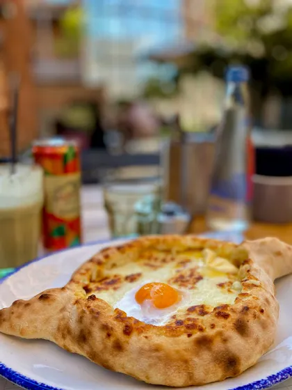 Un pane a forma di barca ripieno di formaggio fuso e un uovo all'occhio di bue, su un piatto su un tavolo all'aperto.