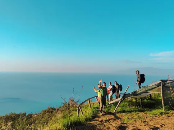 Eine WeRoad Gruppenreise mit Rucksacktouristen, die auf einem Küstenpfad mit Blick auf das blaue Meer unter klarem Himmel posieren.