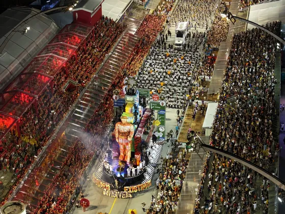 Una vista aérea de un gran desfile de carnaval de noche, con una carroza elaborada avanzando por una calle llena de espectadores.