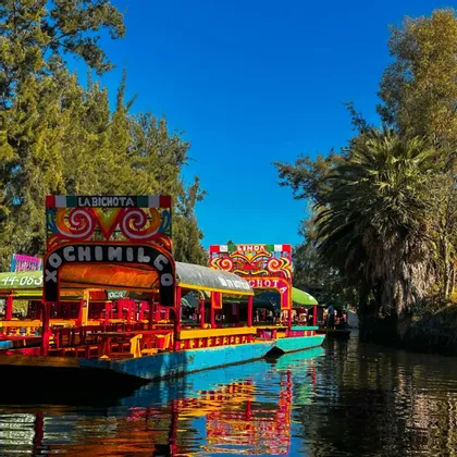 Bunte Boote mit Verdecken treiben auf einem ruhigen Kanal neben üppig grünen Bäumen.
