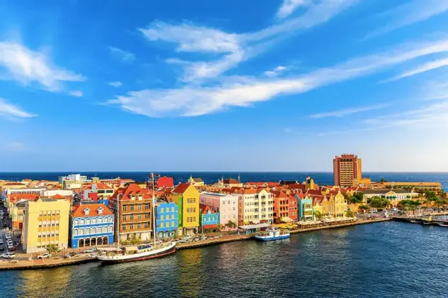 Un paesaggio urbano di edifici colorati lungo un lungomare, con barche ormeggiate nel porto e l'oceano sullo sfondo.