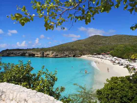 Una vista mozzafiato di una caletta tropicale con persone che nuotano in acqua turchese e si rilassano su una spiaggia di sabbia bianca.