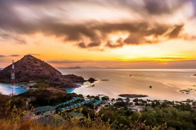 Vue en plongée à longue exposition d'une ville côtière et d'une grande colline près d'une baie au coucher de soleil doré.