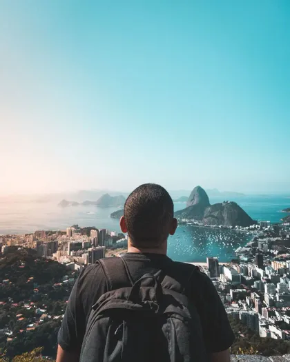 Una persona con uno zaino ammira una vista panoramica di una città costiera e una baia con montagne.