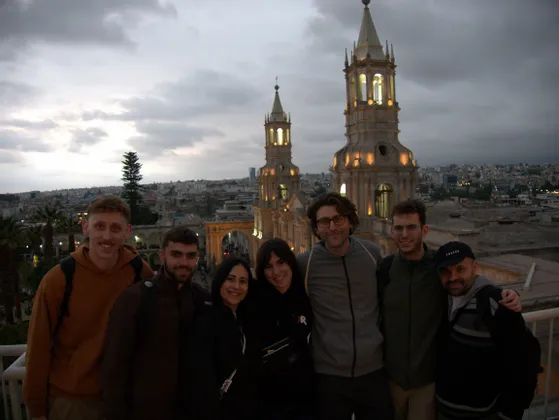 Un viaggio di gruppo WeRoad di sette persone in posa su un punto panoramico con due torri di cattedrale illuminate e uno skyline della città al tramonto.