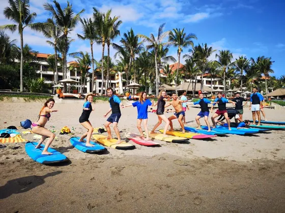 Eine WeRoad Gruppenreise mit einer Surfstunde an einem Sandstrand, wo unter Palmen auf bunten Surfbrettern geübt wird.