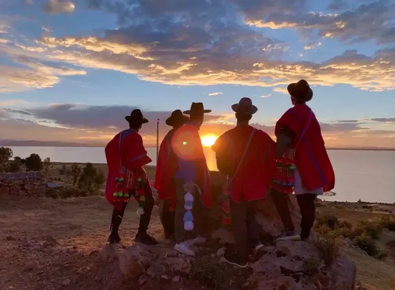 Un viaggio di gruppo WeRoad con poncho e cappelli rossi osserva il tramonto su un lago da uno sperone roccioso.