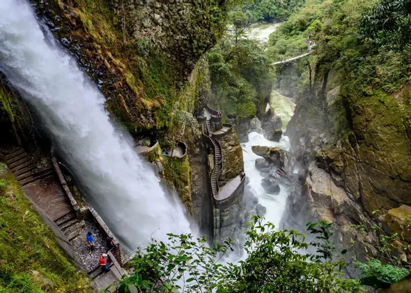 Un grupo de personas de un viaje de WeRoad en una empinada y sinuosa escalera de piedra junto a una gran cascada en un desfiladero rocoso y verde.