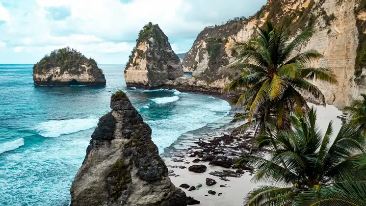 Une vue sur une crique tropicale avec des eaux turquoise, une plage de sable blanc et de grandes formations rocheuses verdoyantes.