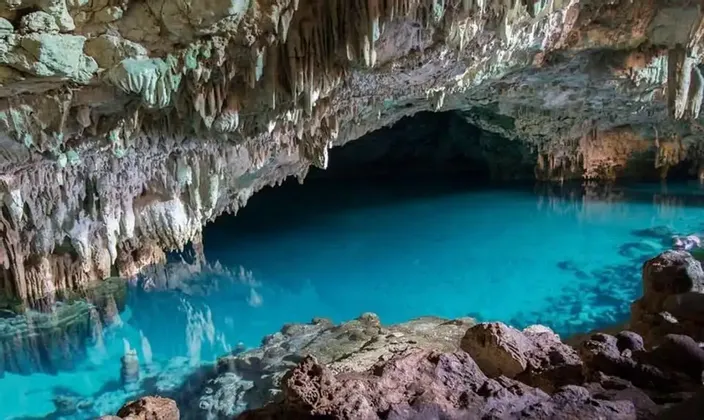 Une grande caverne souterraine abritant un bassin d'eau turquoise limpide, avec de nombreuses stalactites pendant du plafond.